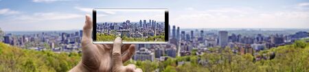 Two hands holding a mobile Smartphone and take a picture of Skyline Panorama from city of Montreal