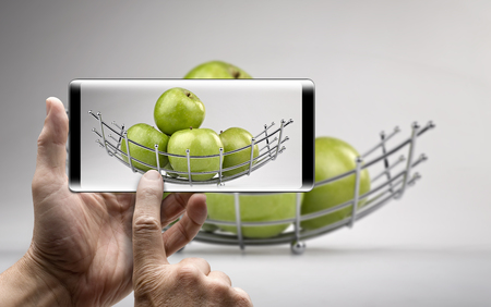 Two hands holding a mobile Smartphone and take a picture of a Modern fruit basket with green applesの写真素材