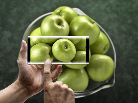 Two hands holding a mobile Smartphone and take a picture of  green applesの写真素材