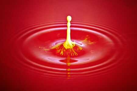 Yellow Ink drop in red water _ close upの写真素材