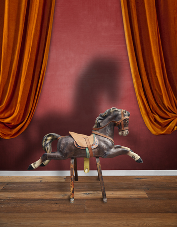 Vintage wooden children horse with his strong shadow against textured red wallの写真素材