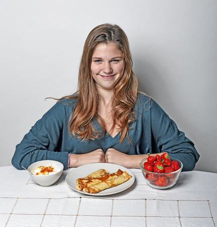 Cute girl sitting at breakfast table eating pancakes and strawberriesの写真素材