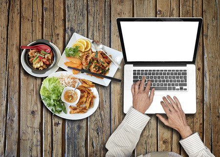 Businessman wearing a white shirt and green tie working on his laptop on rustic wooden table and asian foodの写真素材