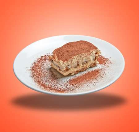 Floating white plate with sweet italian tiramisu dessert on orange gradient backgroundの写真素材