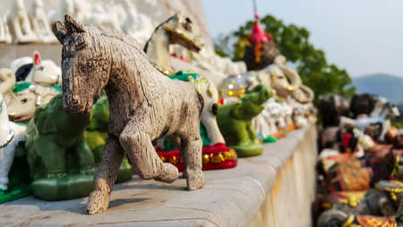 Old handmade wooden figurine of horse, small handicraft wooden horse stand at spirit house on marble ground in evening before sunsetの写真素材