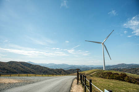 Crossing the road across the green meadow with Wind turbinesの写真素材