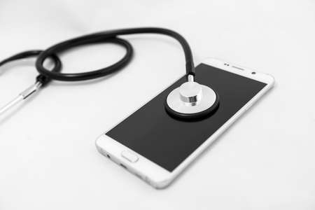 Medical stethoscope tool over the surface of a mobile smart phone, composition isolated over the white backgroundの写真素材