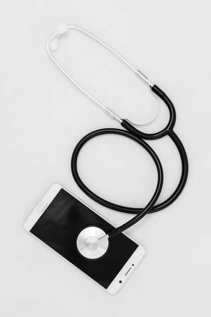 Medical stethoscope tool over the surface of a mobile smart phone, composition isolated over the white backgroundの写真素材