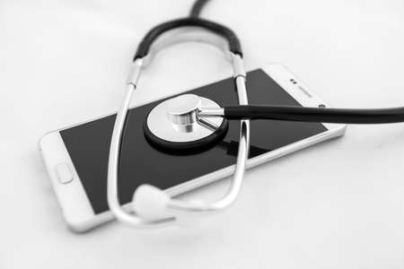 Medical stethoscope tool over the surface of a mobile smart phone, composition isolated over the white backgroundの写真素材