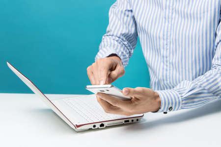 Male hands, Notebook and smart-phones for business in the office on blue background