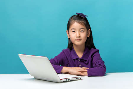 Cute asia little girl who enjoy the laptop computer on blue backgroundの写真素材