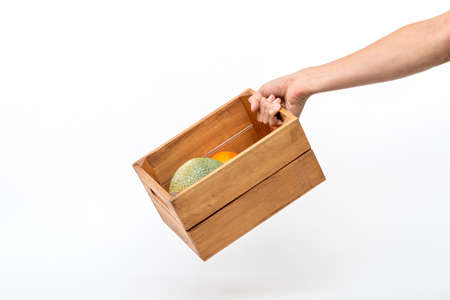 A man's hand holding a wooden box containing melons and oranges. isolated on whiteの写真素材