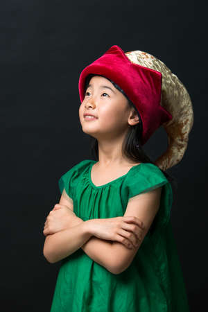 cute asian girl child dressed in fairy hat and green dress on a black background.