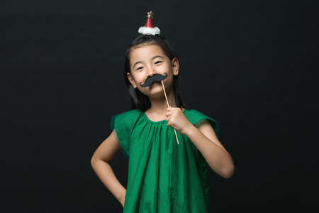 Cute asian woman child with fake mustache and christmas head decoration on black background