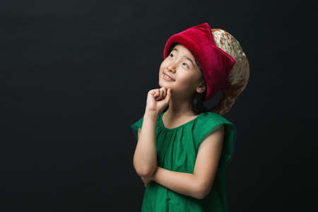 cute asian girl dressed in a green dress with a fairy hat on a black background, with an idea thinking.の写真素材