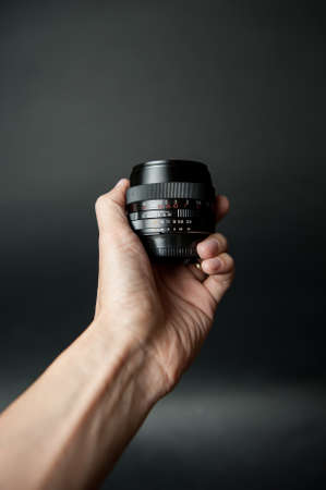 man's hand holding a camera lens on a black backgroundの写真素材