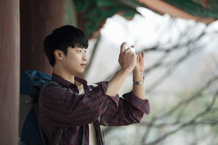 A young man doing a backpacking trip in a Korean traditional house. I'm taking pictures using my smartphone.の写真素材