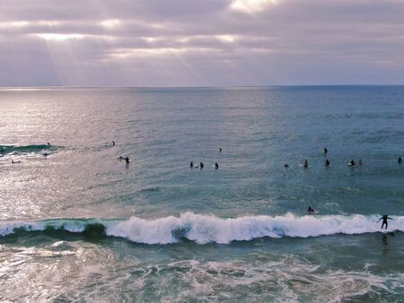 Aerial view of surfers waiting, paddling and enjoying waves before sunset time. Del Mar Beach,...