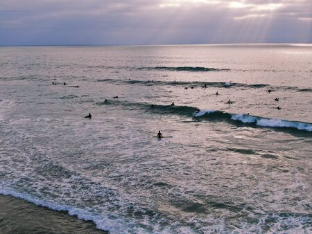Aerial view of surfers waiting, paddling and enjoying waves before sunset time. Del Mar Beach,...