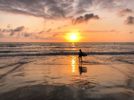 Silhouette of surfer with his board on the beach at Sunset. A man is walking with a surf in his hands across the sea shore during sunset.の写真素材