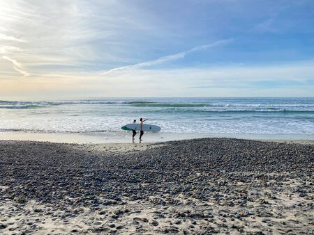 Surfer walking with their boards on Torrey Pines State Beach before sunset twilight, coastal beach...