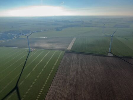 Aerial view of wind turbines on agricultural fields during blue winter day. Energy production with...