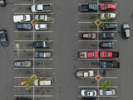 Aerial top view of parking lot at supermarket with with varieties of colored vehicles. People walking to their car and trying to park.の写真素材