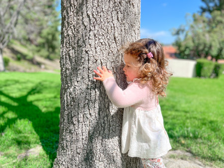 Cute little girl is playing around the grass and trees at the park