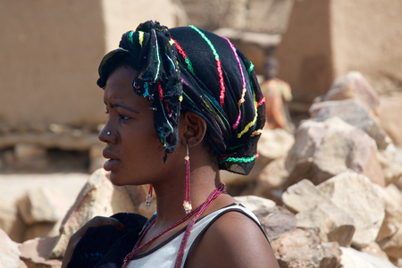 DOUROU, MALI - DEC 30: An unidentified African girl with a headscarf, pendant earrings and necklace watches other kids in her village, on December 30, 2009 near Dourou in the Mopti region of Mali. In this region lives the large majority of the Dogon peoplのeditorial素材