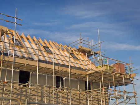 New homes in the process of being constructed, including scaffolding, timber roof trusses and skylights, shown against a blue sky.の写真素材