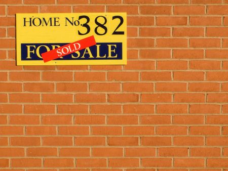 Plot for sale sign on the brick wall of a new home with a sold sticker across the signの写真素材