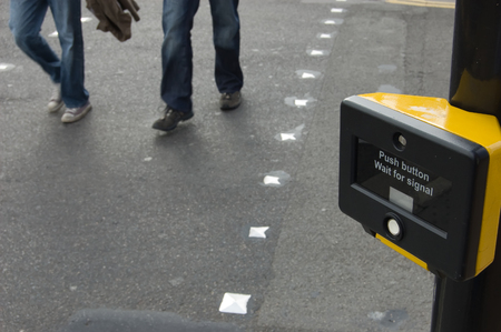 People walking across a pedestrian crossing.  Focus on the crossing sign.の写真素材