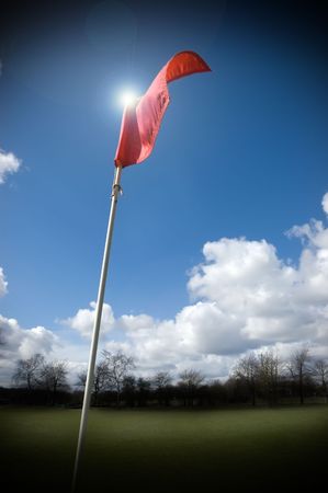 Red golf flag fluttering in the wind lit by the sunの写真素材