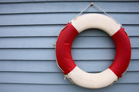 Red and White Lifebuoy hanging on a blue painted wooden fence panel.