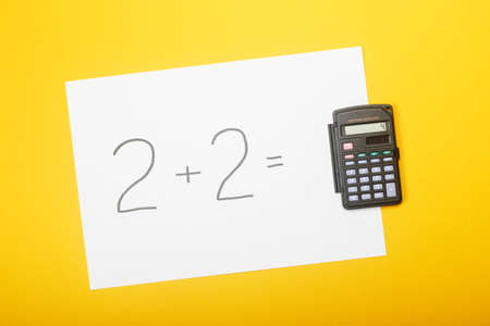Blank paper with task 2 plus 2 and with a solution on calculator on yellow background. Education...