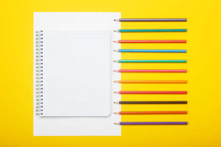 Notebook and color pencils on a yellow background. Mock up with copy space for your ideas. Flat lay...