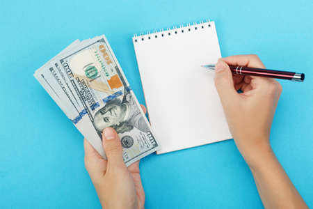 A woman holds money in her hand and writing in a notebook on a blue
