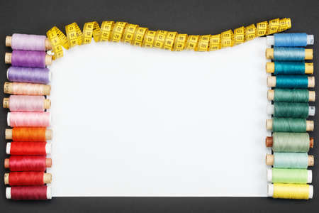 White sheet of paper on a black background with colored thread coils and a tailor meter. The concept...