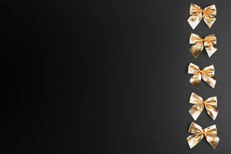 Gold christmas bows on a gradient black background. Holidays mock-up with copy space for your design. Flat layout.の写真素材