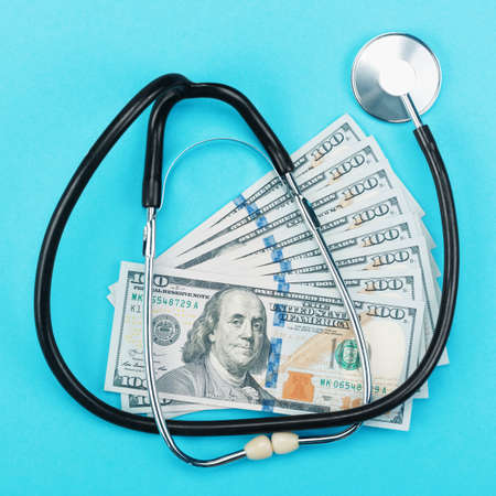 Stethoscope and dollar bills on blue background. Concept of health care costs and medical expenses,...