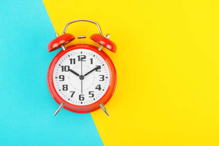 Red retro alarm clock with a big dial, on divided diagonally blue-yellow background. The concept of time, delay, morning rise, the appointed meeting. Layout with copy space for your text. Flat lay.の写真素材