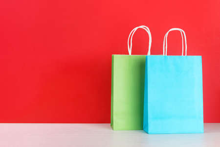 Blue and green shopping or gift bags on wooden desk against red background. The concept of shopping or gifts. Mock-up with a copy space for your text.の写真素材