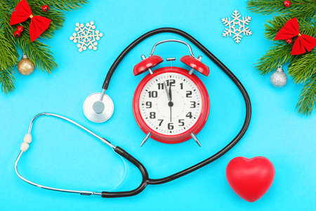 Branches of spruce, christmas toys, red heart with stethoscope and alarm clock with five minutes to...