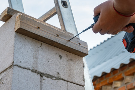 Installation on the wall of a wooden board. Screwing a self-tapping screw into a board. Screwdriver in the hand of the master. Construction site. High quality photoの写真素材