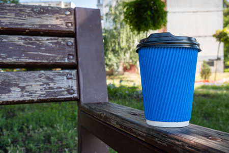 A blue paper coffee cup stands on a wooden street bench. High quality photoの写真素材