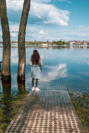 A girl on a flooded shore looks into the distance. The sky is reflected in the water. High quality photoの写真素材