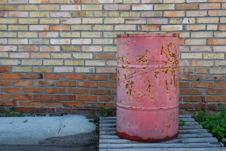 An iron red barrel for storing petroleum products, chemistry stands on a wooden pallet, against a background of a brick wall. High quality photoの写真素材