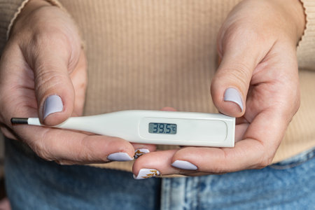 Measured body temperature during illness. In a female hand is a white electronic thermometer a high...