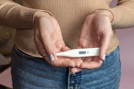 Measured body temperature during illness. In a female hand is a white electronic thermometer a high...