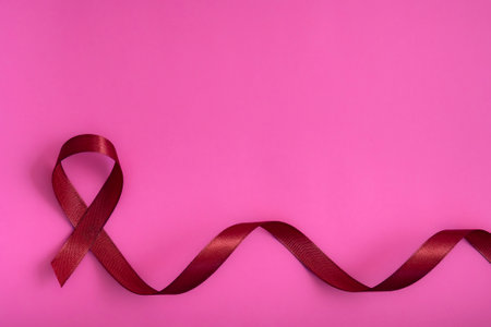 Red ribbon on a pink delicate background, top view with space for text. Campaign to help people facing cancer.の写真素材